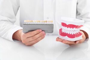 dentist in Katy TX comparing tooth shade guide and denture model during consultation